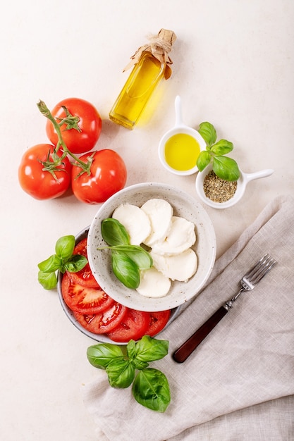 Home made healthy meal concept: cherry tomatoes, mozzarella balls, spices, olive oil and fresh basil. Mozzarella salad over white texture surface. Top view, flat lay