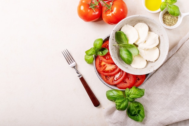 Home made healthy meal concept: cherry tomatoes, mozzarella balls, spices, olive oil and fresh basil. Mozzarella salad over white texture surface. Top view, flat lay