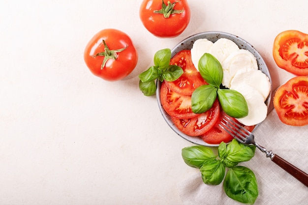 Home made healthy meal concept: cherry tomatoes, mozzarella balls, spices, olive oil and fresh basil. Mozzarella salad over white texture surface. Top view, flat lay