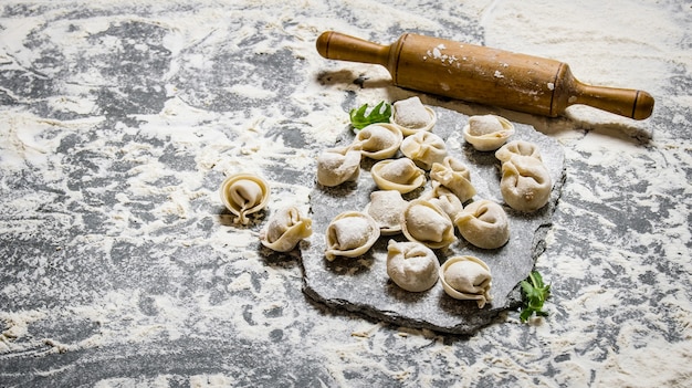 Home-made ravioli with a rolling pin on a stone stand. on stone table with flour.