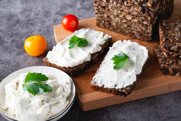 Home made rye bread on a wooden cutting board with curd cheese ricotta and herbs