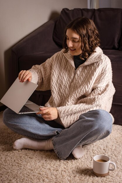 Home Office Bliss Woman working on laptop on soft carpet embracing comfort in winter knitted sweater