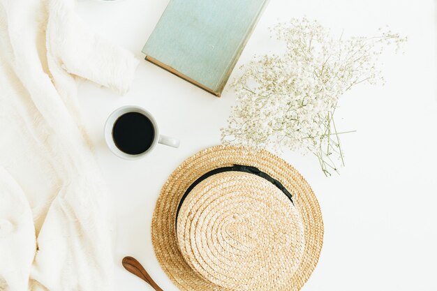 Photo home office desk with coffee, book, straw hat, flowers and blanket on white surface. flat lay, top view