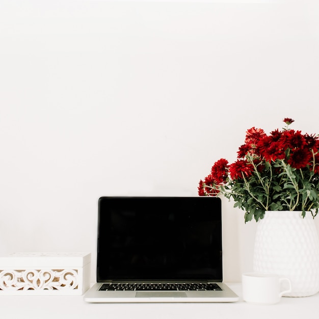 Home office desk with laptop, beautiful red flowers bouquet, white vintage casket in front of white background