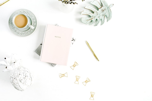 Home office desk. Workspace with pale pastel pink notebook, coffee and decorations on white