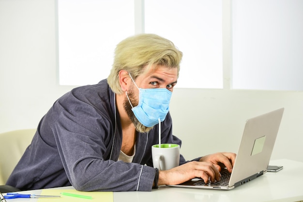 Home office Wearing mask protect from coronavirus Man in mask drink tea coffee using straw Serious hygiene Remote job Worker in medical mask All you need for productive day Totally protected