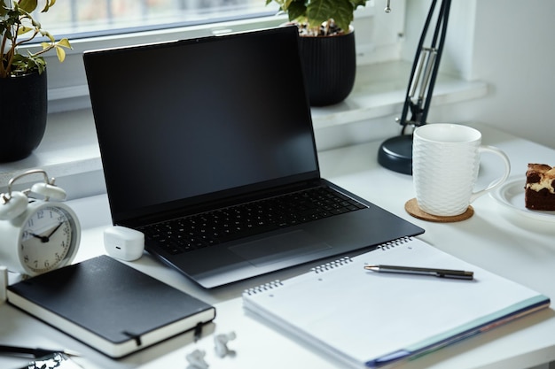 Home office workplace with laptop documents and cup of tea placed on table in front of window remote