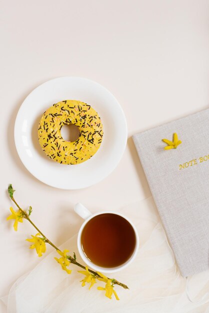 Home office workspace frame with notepad cup of tea donut pen Flat position top view Copy space