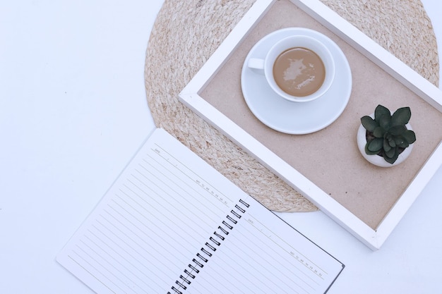 Home office workspace with notebook sheet and cup of coffee in a wooden tray. Flat lay, top view.