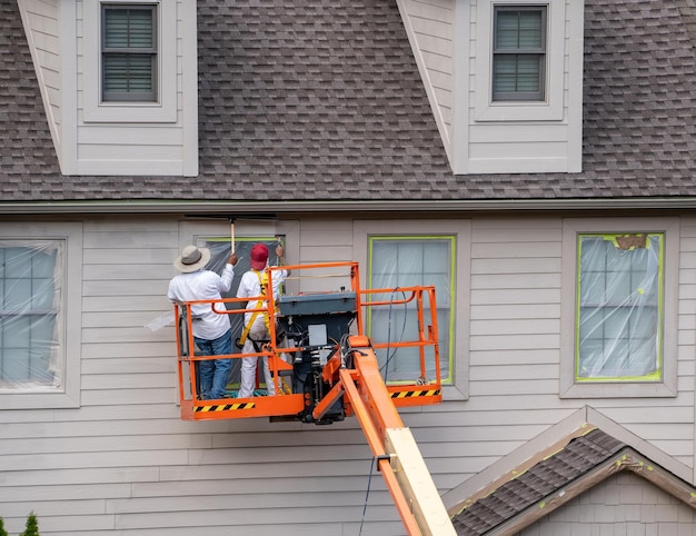 Home painters using paint spray from boom lift