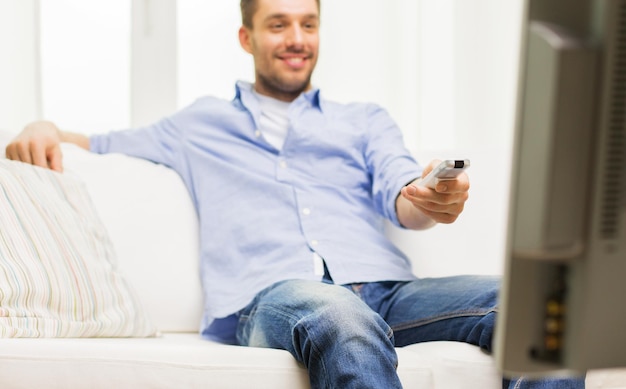 Photo home, people, technology and entertainment concept - close up of man watching tv and changing channels with remote control at home