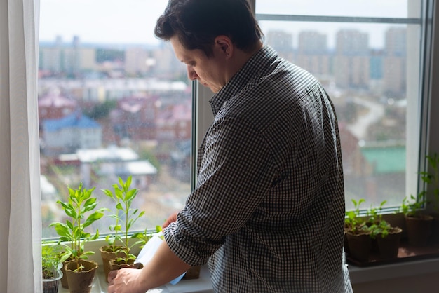 Home plant care concept Young man watering seedlings on the windowsill view from the back