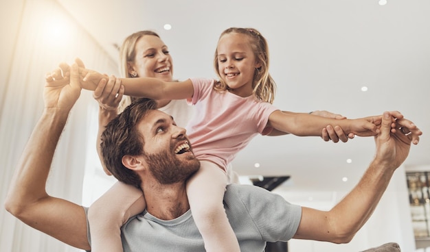 Home playing and family with girl parents and happiness with joy fun and support on a weekend break Child mother and father with kid funny and relax with care smile and cheerful in a lounge