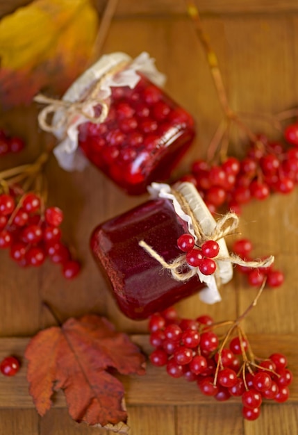 Home preparations Viburnum jam in a glass jar on a wooden table near fresh viburnum berries and autumn berries