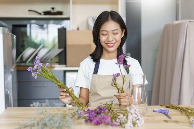 Home relaxation concept Young woman sitting in kitchen room and arrange flowers in vase on table