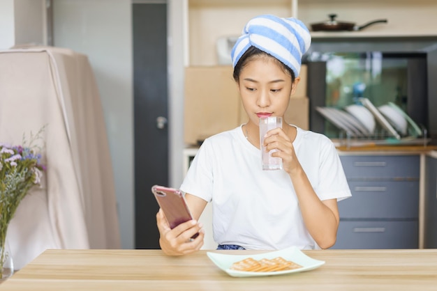 Home relaxation concept Young woman in turban after shower to drinking water and surf social media