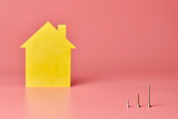 Home repair and redecorated concept. House renovation. Screws and yellow house shaped figure on pink background.