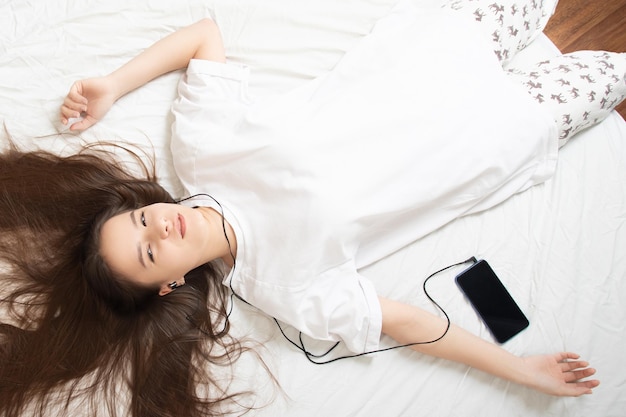 Home rest The girl lies on the bed with a smartphone listens to music with her eyes closed enjoys