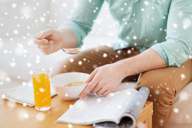 home, rest, news, breakfast and people concept - close up of man reading magazine and eating breakfast at home