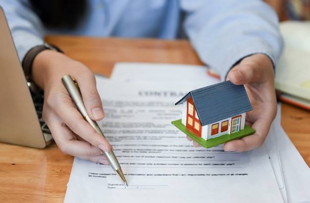 Home salesman holding a pen and model house in hand.