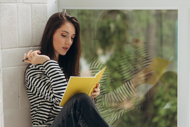 Home schooling A teenager girl a student sits on a windowsill writes homework Distance learning preparation for exams Soft selective focus