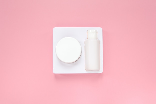 Home skin care system, cream and tonic in white packaging on pastel pink background.