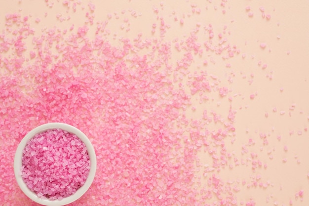 Home spa therapy Top view of white bowl with pink bath salt and crystals scattered over peach background Copy space