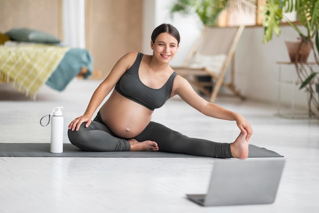 Home Sports Smiling Pregnant Woman Training With Laptop Stretching Leg Muscles