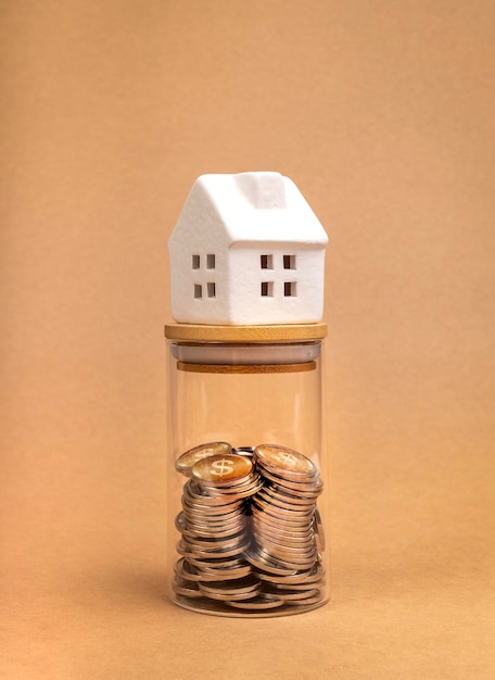 Home Tax property investment and house mortgage financial savings money concepts White miniature house on glass bottle with money coins inside isolate on recycle paper background vertical style