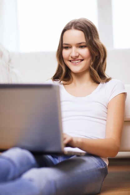 home, technology and internet concept - smiling teenage girl sitting on the floor with laptop computer at home