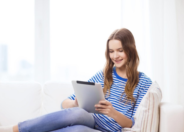 home, technology and internet concept - smiling teenge girl lying on the couch with tablet pc computer at home