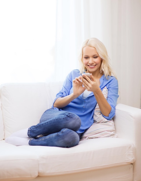 home, technology and internet concept - smiling woman with smartphone sitting on couch at home