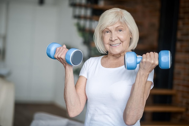 Home workout. Short-haired senior woman exercising with dumbbells