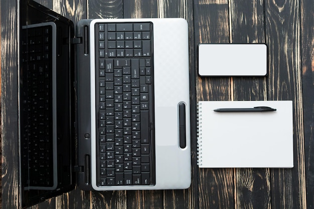 Home workplace Blank notebook laptop pen and mobile on a dark background