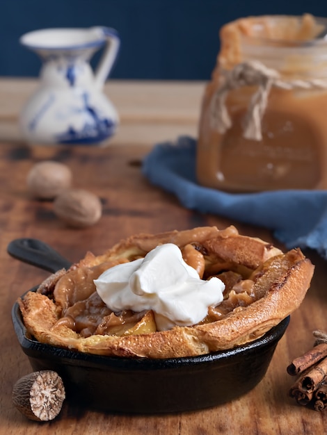 Homemade apple pie with caramel sauce and cream on a wooden table. Close-up. Near a jar of caramel, milk and spices. Tasty dessert.