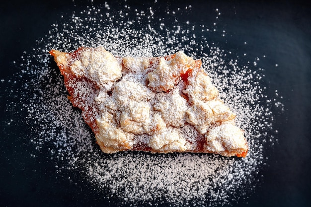 Homemade apricot pie Top view of a slice of rustic hot sweet cake in icing sugar on a black plate