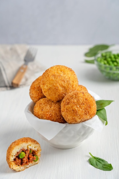 Homemade Arancini Italian or Sicilian rice balls stuffed with mince and green peas in bowl on table