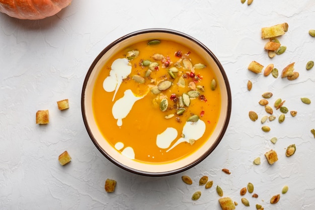 Homemade autumn pumpkin cream soup with cream croutons seeds and basil on a light wooden background