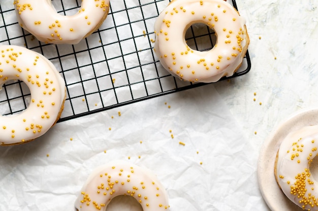 Homemade baked iced donuts with golden pearls on a black rack and on baking paper.