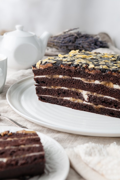 Homemade Banana Cake. With biscuit chocolate cakes. Soaked in butter cream. Garnished with Chocolate. On a white plate. In the background a former teapot and a mug.