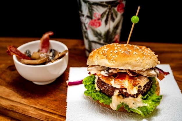 Homemade beef burger with lettuce tomato mushrooms and cheese on a wooden board with black background Chopped view Copy text Fastfood concept