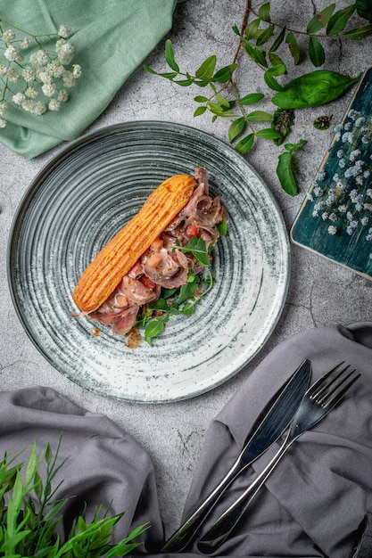 Homemade beef meat sandwich in croissant with lettuce, tomato and arugula leaves in a plate on a gray stone table. Restaurant Menu