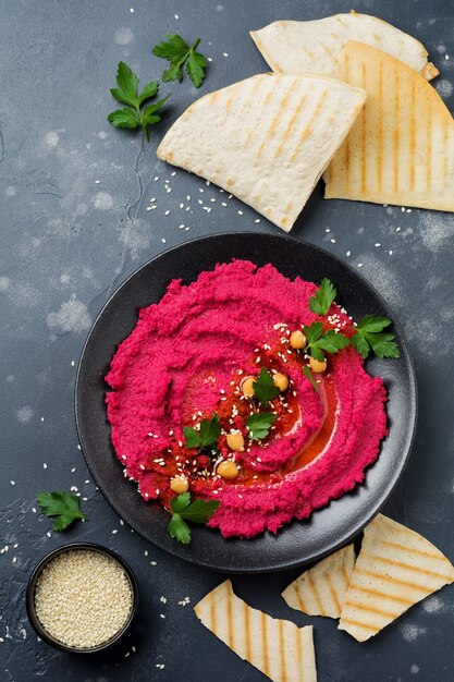 Homemade beetroot hummus in black ceramic dish on old dark concrete.