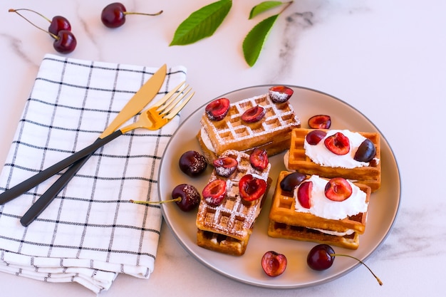 Homemade belgin waffles whith whipped cream and cherries served on a plate for breakfast.