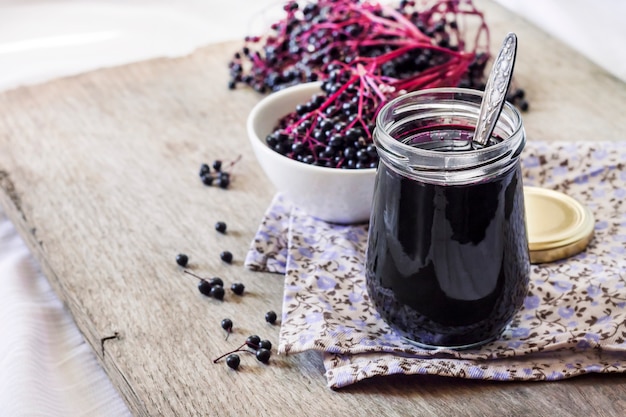 Homemade black elderberry syrup in glass jar and bunches of black elderberry