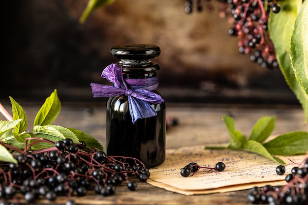 Homemade black elderberry syrup recipe in a glass bottle on a wooden table. Fresh berries in the background. Copy space