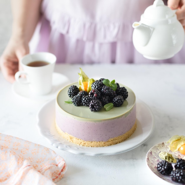 Homemade blackberry cheesecake and matcha tea on the festive table The girl pours tea Square