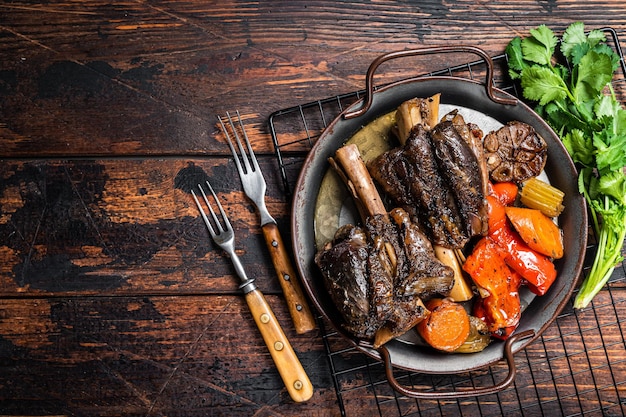 Homemade Braised Lamb Shanks with Sauce and Herbs in a steel tray Wooden background Top view Copy space