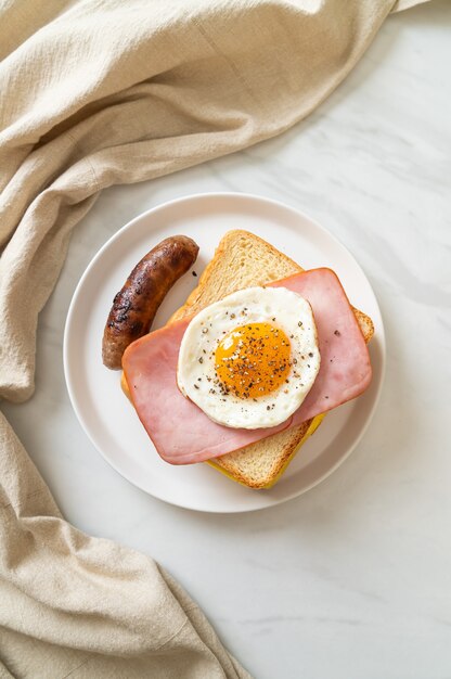 homemade bread toasted cheese topped ham and fried egg with pork sausage for breakfast