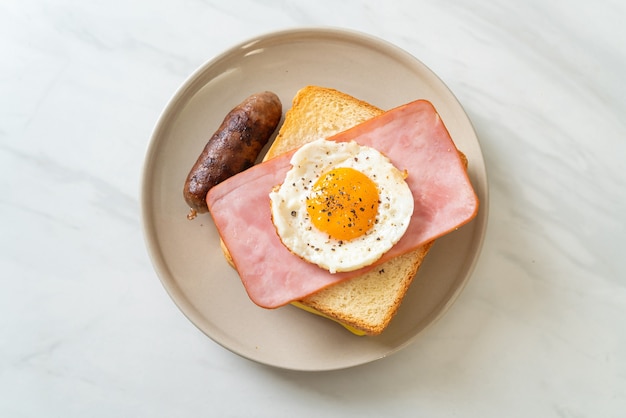 homemade bread toasted cheese topped ham and fried egg with pork sausage for breakfast